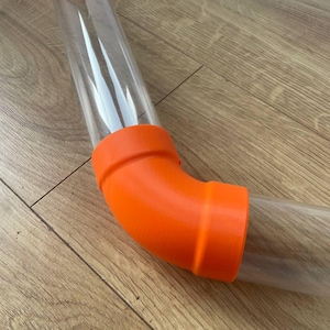 May include: Clear plastic tubing with an orange elbow joint. The tubing is curved and appears transparent. The elbow joint is a bright orange colour and connects two sections of the tubing.