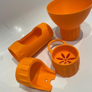May include: A collection of vibrant orange kitchen utensils, including a funnel, a strainer with a handle, and two cylindrical parts. The items are made of a textured plastic material and are arranged on a white surface.