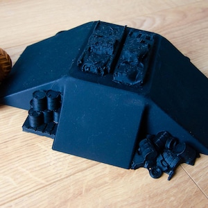 May include: A black plastic ramp with two small black toy tanks on top. The ramp has a black plastic base with a pile of small black barrels on the side.