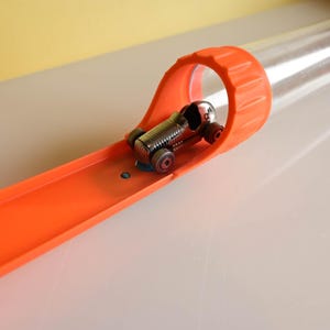 May include: A miniature silver race car on an orange track with a clear plastic tube. The track has a loop-de-loop design. The toy car has red wheels and is ready to race.