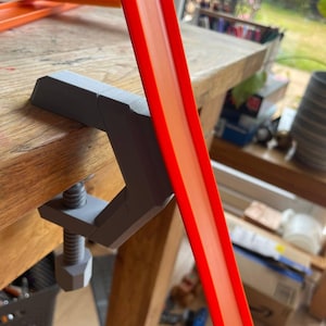 May include: A grey 3D printed clamp holding a bright orange plastic track piece. The track piece is angled upwards and has a small hole in the top.