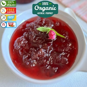 Könnte beinhalten: Eine weiße Schüssel gefüllt mit leuchtend roter Hagebuttenmarmelade, gekrönt von einer einzelnen rosa Rose und einem grünen Minzblatt. Der Text "100% Organic Natural Product" ist in der oberen rechten Ecke des Bildes sichtbar.