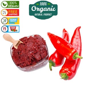 Puede incluir: Un cuenco de vidrio lleno de una pasta marrón rojiza y una pequeña cuchara de madera. Tres pimientos rojos brillantes están a la derecha. La imagen incluye texto que dice "100% Vegano", "Envío gratis", "Calidad premium", "Regalo gratis" y "100% Organic Natural Product".