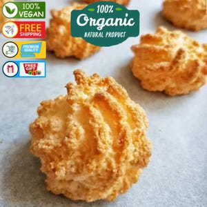 Op de afbeelding: Close-up van verschillende goudbruine kokosmacarons. De koekjes hebben een textuur, grillig oppervlak. De afbeelding bevat ook de tekst "100% Vegan", "Gratis verzending", "Premium kwaliteit", "Gratis cadeau" en "100% Organic Natural Product".