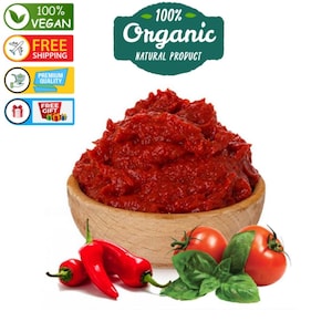 Op de afbeelding: Een houten kom gevuld met levendige rode tomatenpuree, vergezeld van verse rode chilipepers, rijpe tomaten en basilicumbladeren. De afbeelding bevat labels die aangeven dat het product 100% biologisch en veganistisch is.