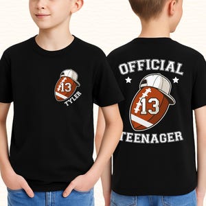 May include: Black t-shirt featuring a football graphic with the number 13 and the name "Tyler". The back of the shirt reads "OFFICIAL TEENAGER" above the same football graphic. The design includes a white baseball cap.