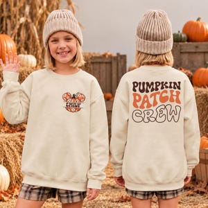 May include: A beige crewneck sweatshirt featuring a small graphic on the front left chest of a pumpkin with mouse ears and the name EMILY. The back displays the large brown and orange text PUMPKIN PATCH CREW in a wavy, retro-style font.