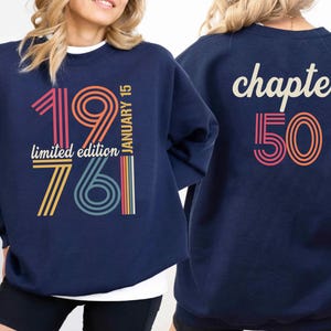 May include: Navy blue sweatshirt with the text "1976 January 15 limited edition 761" on the front and "chapter 50" on the back. The text is in a retro color scheme of pink, orange, yellow, and teal.