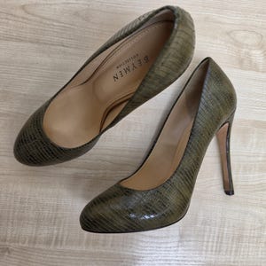 Op de afbeelding: Een paar olijfgroene pumps met hoge hakken en een gestructureerd, op reptielen geïnspireerd patroon. De binnenkant van de schoen heeft een beige voering met de tekst BEYMEN COLLECTION in het zwart gedrukt. De schoenen hebben een ronde neus en een slanke naaldhak.
