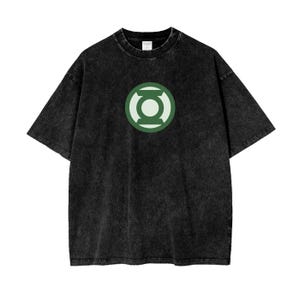 Puede incluir: Una camiseta de manga corta negra con efecto lavado al ácido que presenta un logotipo circular de Green Lantern centrado en el pecho. El gráfico consiste en un círculo verde oscuro con un símbolo de linterna verde claro. Cuello redondo.