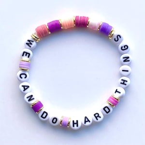 May include: White beaded bracelet with the words "We Can Do Hard Things" in black lettering. The beads are interspersed with pink, purple, and gold beads.