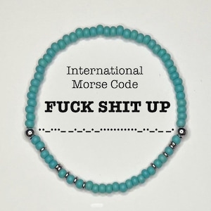May include: A turquoise beaded bracelet with the text "International Morse Code" and "FUCK SHIT UP". The Morse code for the phrase is displayed below the text. The bracelet has silver-colored accents.