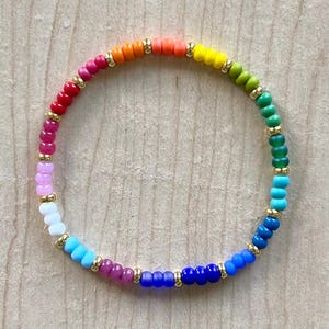 May include: A rainbow-colored beaded bracelet with gold-colored accents. The bracelet features a spectrum of colors, including red, orange, yellow, green, blue, and purple. The beads are strung together with gold-colored spacers.