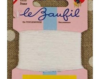 May include: A spool of white thread labeled "le Zaufil" in cursive script, with "Lille France" and "Fabrication française" on the pink packaging. The packaging has a yellow stripe and a blue stripe. The background is a brown fabric with white polka dots.