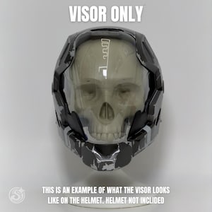 Puede incluir: Una visera negra y plateada unida a un casco con una placa frontal en forma de calavera. El texto VISOR ONLY aparece en la parte superior, y THIS IS AN EXAMPLE OF WHAT THE VISOR LOOKS LIKE ON THE HELMET. HELMET NOT INCLIDED en la parte inferior.