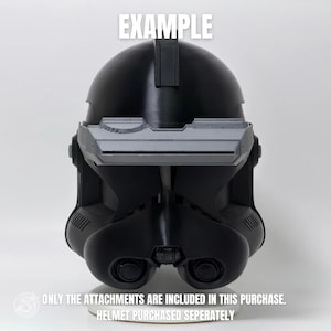Puede incluir: Un casco negro con accesorios grises, con visera y aberturas para los ojos. La palabra "EXAMPLE" está impresa en la parte superior. El texto en la parte inferior dice "ONLY THE ATTACHMENTS ARE INCLUDED IN THIS PURCHASE. HELMET PURCHASED SEPERATELY."