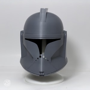 May include: A gray, plastic helmet with a distinctive visor and a rounded top. The helmet has a detailed design, including a central ridge and side panels. It is displayed on a white stand against a white background.