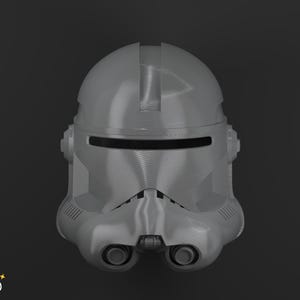 Op de afbeelding: Een grijze plastic helm met een vizier en twee cirkelvormige kenmerken eronder. De helm heeft een glad, reflecterend oppervlak en is ontworpen met een reeks ventilatieopeningen en ribbels. De helm is een replica van een Star Wars-personage.