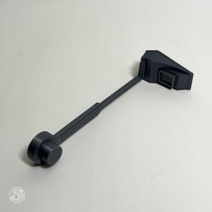 May include: A dark gray, 3D-printed tool with a cylindrical end, a long, slender handle, and a rectangular head. The tool is designed for a specific function, likely for a mechanical or technical application. The design is modern and minimalist.