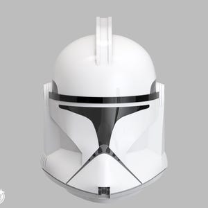 Könnte beinhalten: Ein weiß-schwarzer Helm mit markantem Design, mit einem zentralen vertikalen Grat und einem schwarzen Visierbereich. Der Helm hat eine glatte, glänzende Oberfläche und ist vor einem neutralen grauen Hintergrund platziert.