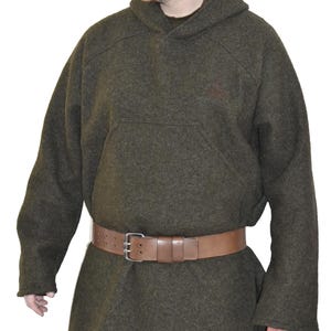 Op de afbeelding: Een donkergroene tuniek met capuchon, kangoeroezak en lange mouwen. Een bruine leren riem wordt om de taille gedragen. De persoon draagt een donkergroene baseballcap.