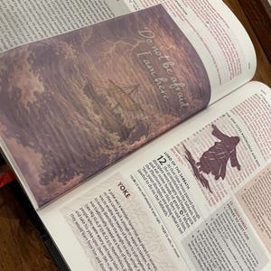 May include: Open Bible with a bookmark featuring an illustration of a ship in a storm with the text "Do not be afraid, I am here". The Bible is open to a page with text.
