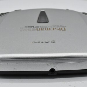 May include: Silver Sony Discman ESP2 CD player. The portable CD player has a black top button and a headphone jack. The text "Discman ESP2" and "SONY" are visible on the device. A classic portable CD player.