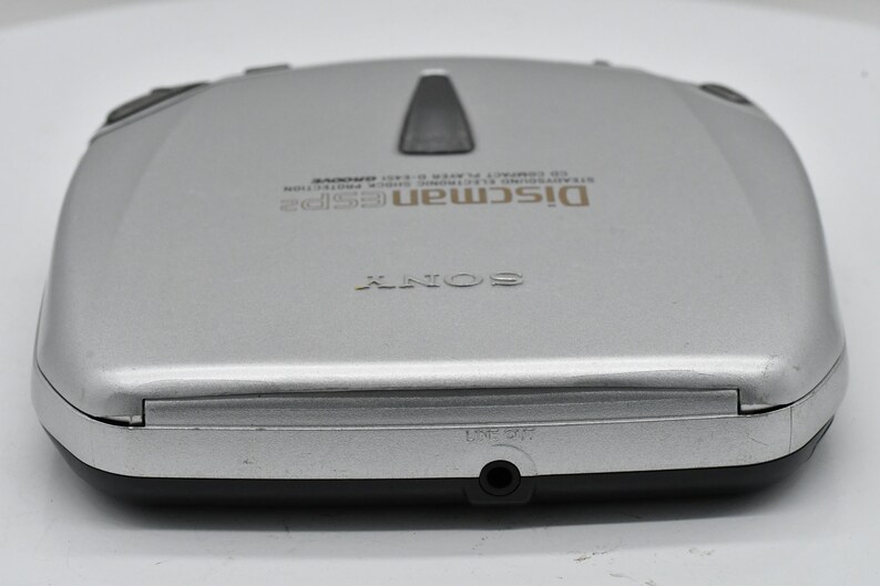May include: Silver Sony Discman ESP2 CD player. The portable CD player has a black top button and a headphone jack. The text "Discman ESP2" and "SONY" are visible on the device. A classic portable CD player.