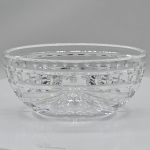 May include: A clear, cut-glass bowl with a round shape. The bowl features intricate patterns around the sides and a starburst design on the bottom. The glass reflects light, creating a sparkling effect.