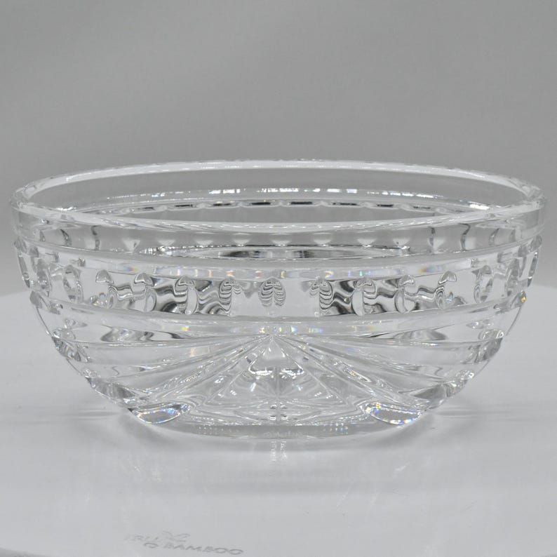 May include: A clear, cut-glass bowl with a round shape. The bowl features intricate patterns around the sides and a starburst design on the bottom. The glass reflects light, creating a sparkling effect.