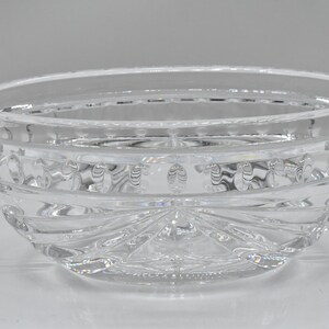 May include: A clear, decorative glass bowl with a rounded shape. The bowl features intricate etched patterns around the sides and a starburst design on the base. The bowl is made of clear glass.