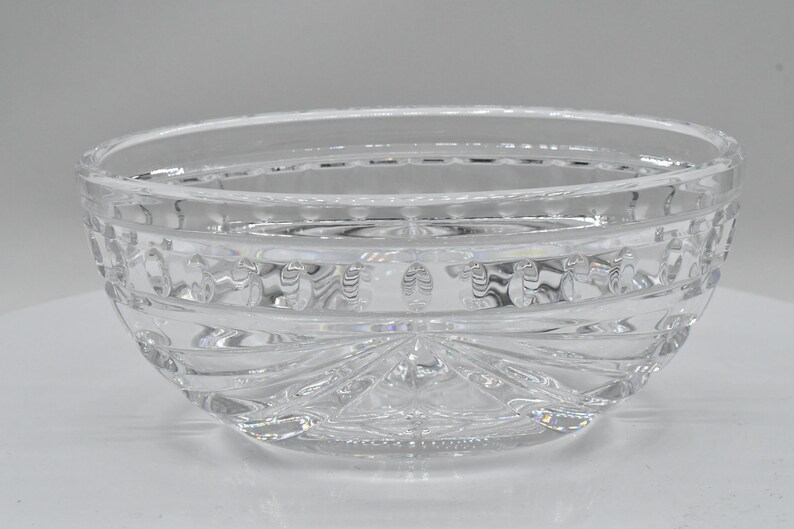 May include: A clear, decorative glass bowl with a rounded shape. The bowl features intricate etched patterns around the sides and a starburst design on the base. The bowl is made of clear glass.