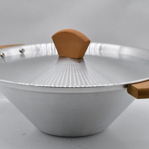 May include: A silver-colored wok with a matching lid and wooden handles. The lid has a wooden handle on top. The wok is designed with a wide, sloped bowl and is suitable for cooking various Asian-inspired dishes.