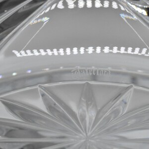 May include: Close-up of a clear crystal bowl with a starburst pattern on the base. The bowl has a series of vertical cuts and a decorative rim. The word "Cartines" is etched into the glass.