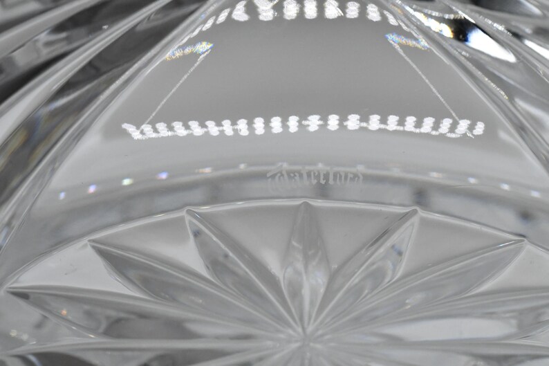 May include: Close-up of a clear crystal bowl with a starburst pattern on the base. The bowl has a series of vertical cuts and a decorative rim. The word "Cartines" is etched into the glass.