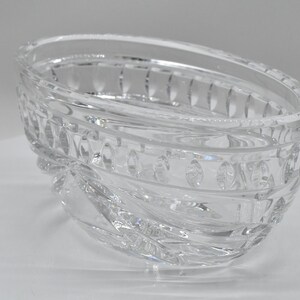 May include: Clear, oval-shaped crystal bowl with a decorative, textured design. The bowl features a series of oval and rectangular patterns around the rim and sides. The crystal bowl is a decorative item.
