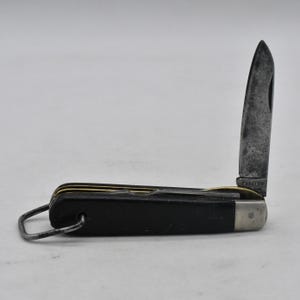 May include: A black pocket knife with a partially open blade. The knife has a black handle with a gold accent and a silver loop for attaching to a keychain. The blade is silver and has the word "CABELLUS" printed on it.