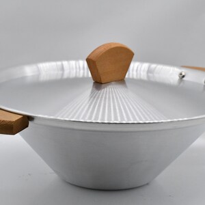 May include: A silver-colored wok with a matching lid and wooden handles. The lid has a wooden knob. The wok is designed with a wide, sloped bowl and is suitable for stir-frying and other cooking methods.