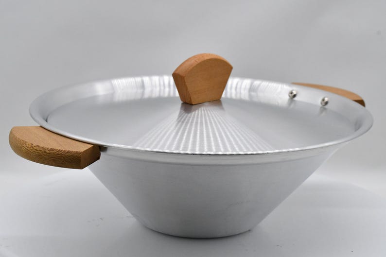 May include: A silver-colored wok with a matching lid and wooden handles. The lid has a wooden knob. The wok is designed with a wide, sloped bowl and is suitable for stir-frying and other cooking methods.