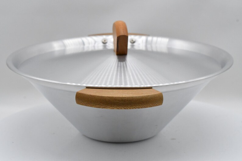 May include: A silver wok with a matching lid and wooden handles. The wok has a wide, conical shape and a lid with a wooden handle. The handles are made of light-colored wood. The wok is designed for cooking.
