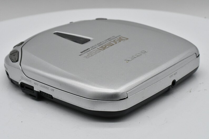 May include: Silver Sony Discman portable CD player. The device has a rectangular shape with rounded edges and a black base. The top of the player has the word "Discman" printed on it.