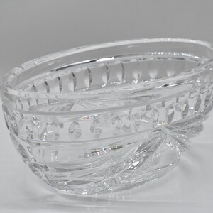 May include: Clear, oval-shaped crystal bowl with intricate cut glass detailing. The bowl features a decorative pattern around the rim and a starburst design at the base. A decorative piece for serving or display.