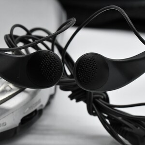 May include: Black over-the-ear headphones with a silver audio device in the background. The headphones have a classic design with ear speakers and a wired connection. The ear speakers have a textured surface.
