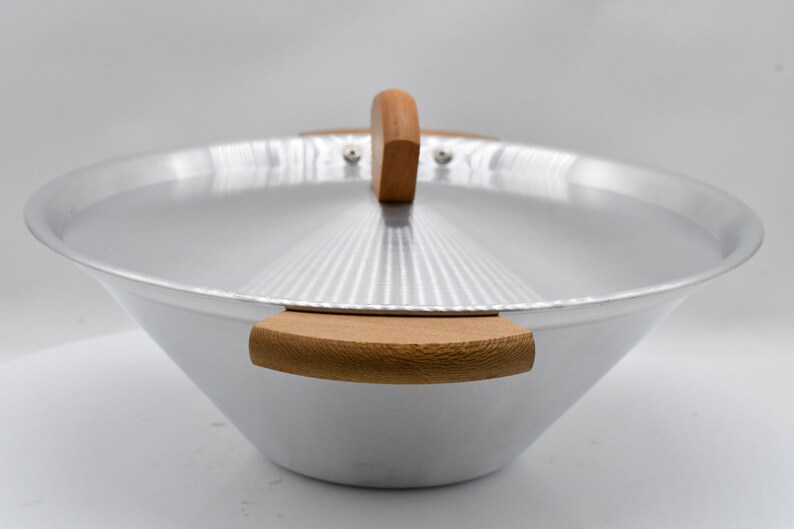 May include: A silver-colored wok with a wooden handle and two wooden side handles. The lid has a wooden handle and a ridged design. The wok is set against a white background.