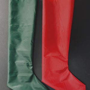 May include: Two Christmas stockings, one green and one red, are laid out on a black surface. The stockings are made of a smooth, shiny fabric.