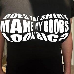 May include: Black t-shirt with the white text: "DOES THIS SHIRT MAKE MY BOOBS LOOK BIG?" The text is curved to fit the shape of the chest. The shirt is made of a soft material.