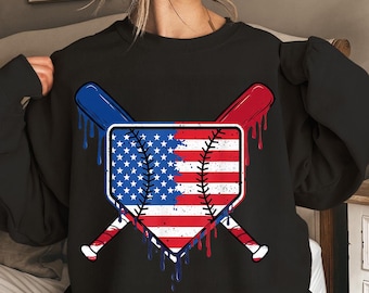 May include: Black sweatshirt with a baseball home plate design. The home plate is split in half, with the American flag on each side. Two baseball bats are crossed behind the home plate, with red, white, and blue dripping paint.