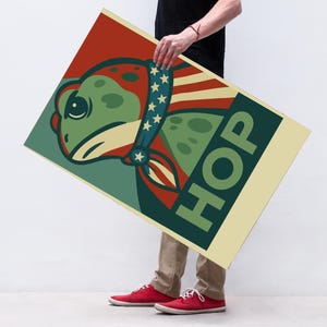 May include: A poster featuring a cartoon frog wearing a patriotic bandana with stars and stripes. The frog is green with red and blue accents, and the word "HOP" is printed in large green letters on a cream background.