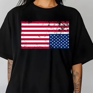 Può includere: Una maglietta nera con un design di bandiera americana rovinato. La bandiera è capovolta, con le stelle sulla metà inferiore.