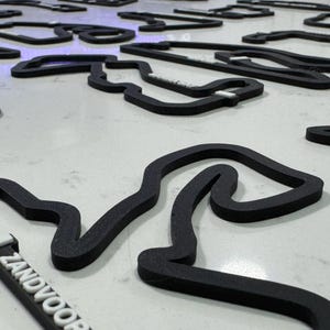 May include: A collection of black race track outlines, each with a unique shape. One outline has the name "Zandvoort" printed on it in white.